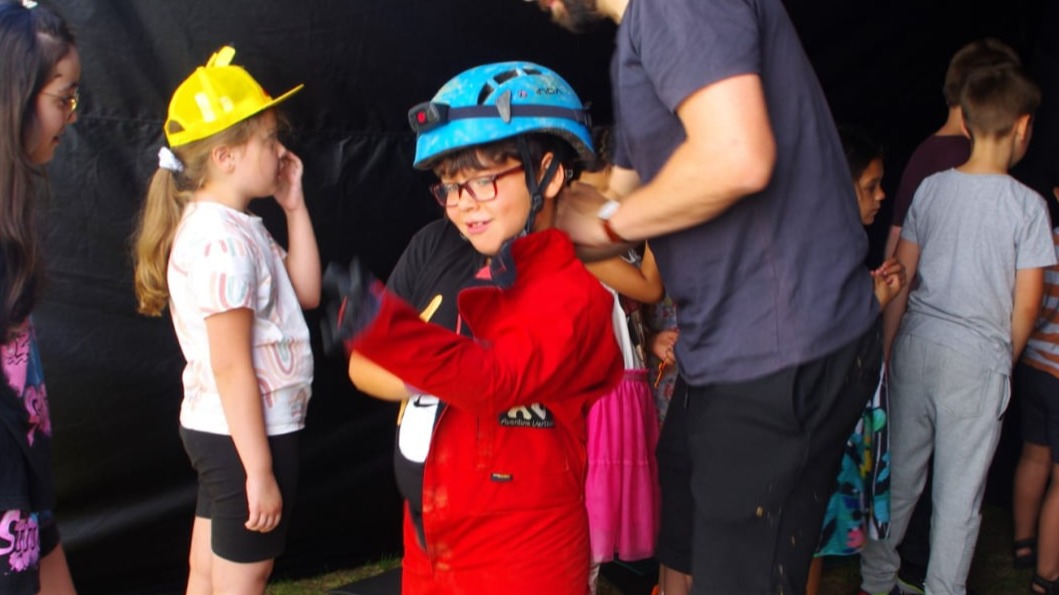 Kinder probieren einen Schutzanzug und Helme für Höhlenerkundung an